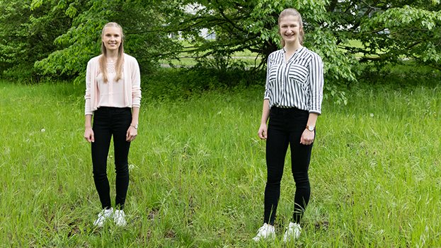 Emily Narten und Anja Tiede stehen mit Abstand auf einem Stück Rasen mit grünen Büschen im Hintergrund.