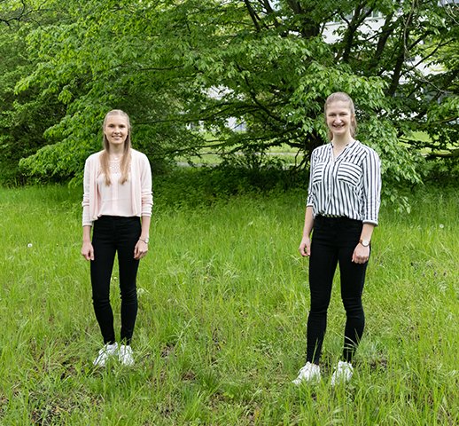 Emily Narten und Anja Tiede stehen mit Abstand auf einem Stück Rasen mit grünen Büschen im Hintergrund.