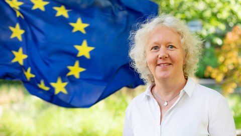 Eine Frau steht vor einer Flagge der Europäischen Union.