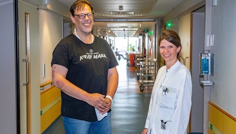 Patient Dirk P. steht neben seiner behandelnden Ärztin Dr. Ramona Schuppner auf einem Stationsflur der MHH. 