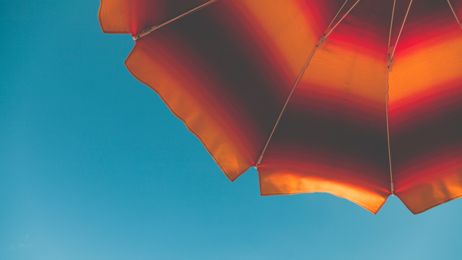 Ausschnitt eines aufgespannten orange-rot-braunen Sonnenschirmes vor blauem Himmel