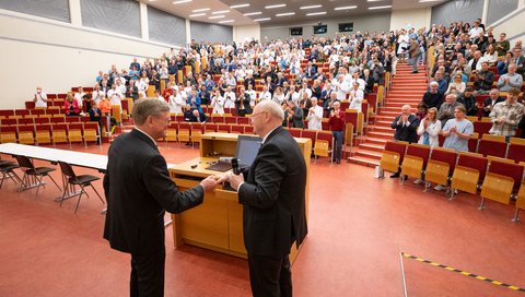 In einem MHH-Hörsaal sitzen viele Menschen und applaudieren Prof. Haverich, der mit Prof. Manns vorne vor den Sitzreihen steht. 