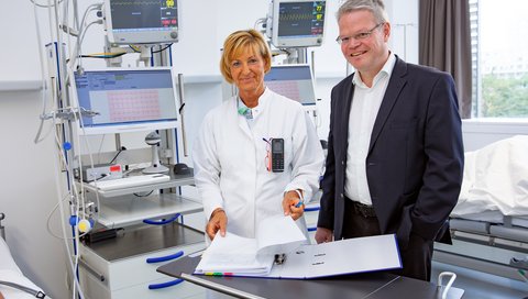 Professor Dr. Christoph Schindler und Carola Westenberg stehen in einem Patientenzimmer des Zentrums für klinische Studien.