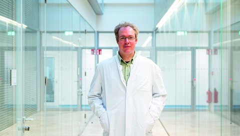 Der Herpesvirus-Forscher Professor Dr. Thomas Krey steht in einem Gang der Universität Lübeck.