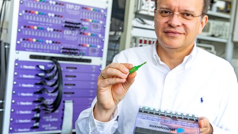 Professor Dr. Andrej Kral steht mit einem Multi-Elektroden-Array in der Hand vor einem Verstärker zur Hirnstrommessung.