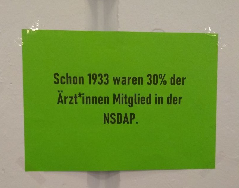 Grüner Zettel mit bedruckter Aufschrift: Schon 1933 waren 30% der Ärzt*innen Mitglied in der NSDAP