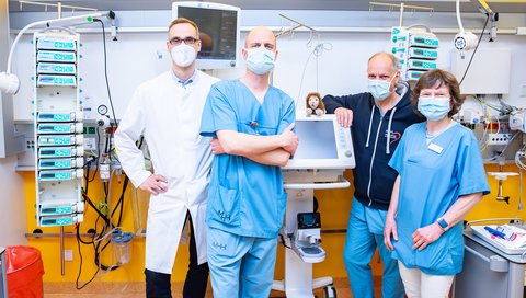 Dr. Bernd Auber, Dr. Alexander von Gise und Dr. Michael Sasse von der intensivmedizinischen Station sowie Professorin Dr. Bettina Bohnhorst von der neonatologischen Station stehen in einem Patientenzimmer der Kinderklinik. 