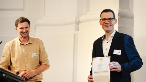 Prof. André Bleich erhält eine urkunde und lächelt in die Kamera