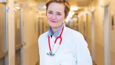 Porträtbild von Prof. Dr. med. Christine Happle, die in weißem Arztkittel in einem Stationsflur steht.