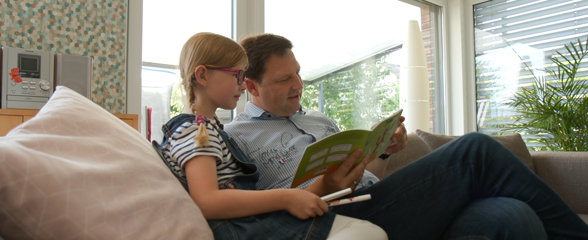Julia und ihr Vater sitzen auf dem Sofa. Ihr Vater hält ein Buch in der Hannd. Copyright: MHH