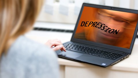 Eine Person sieht auf einen Bildschirm, auf dem groß das Wort „Depression“ erscheint.
