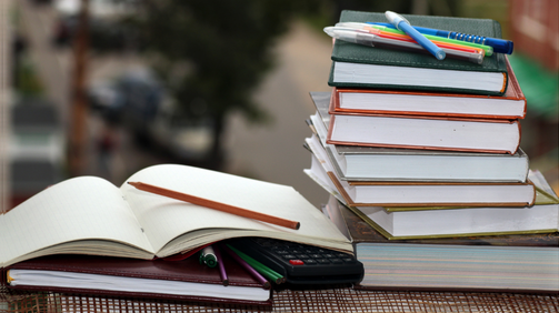 A stack of books, one open and pencils ontop of the books.