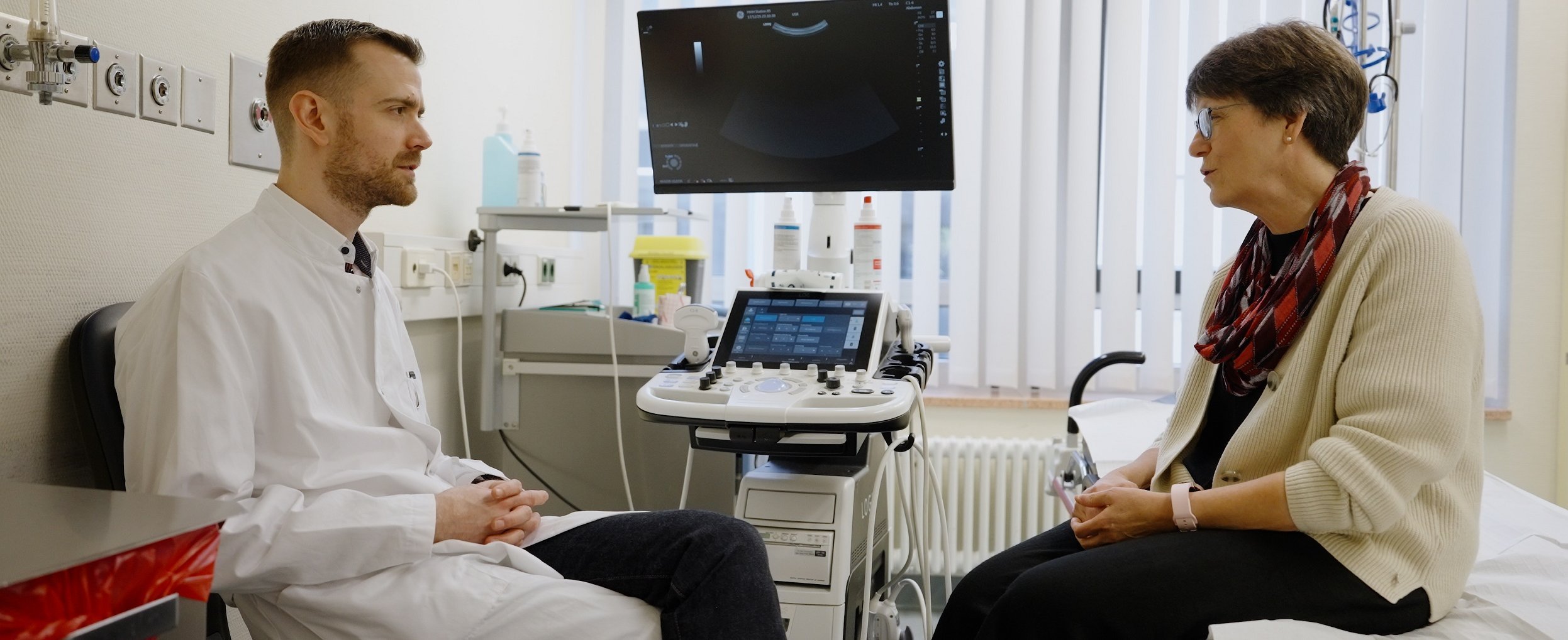 Ein Arzt und eine Patientin sitzen sich in einem Behandlungszimmer gegenüber. 