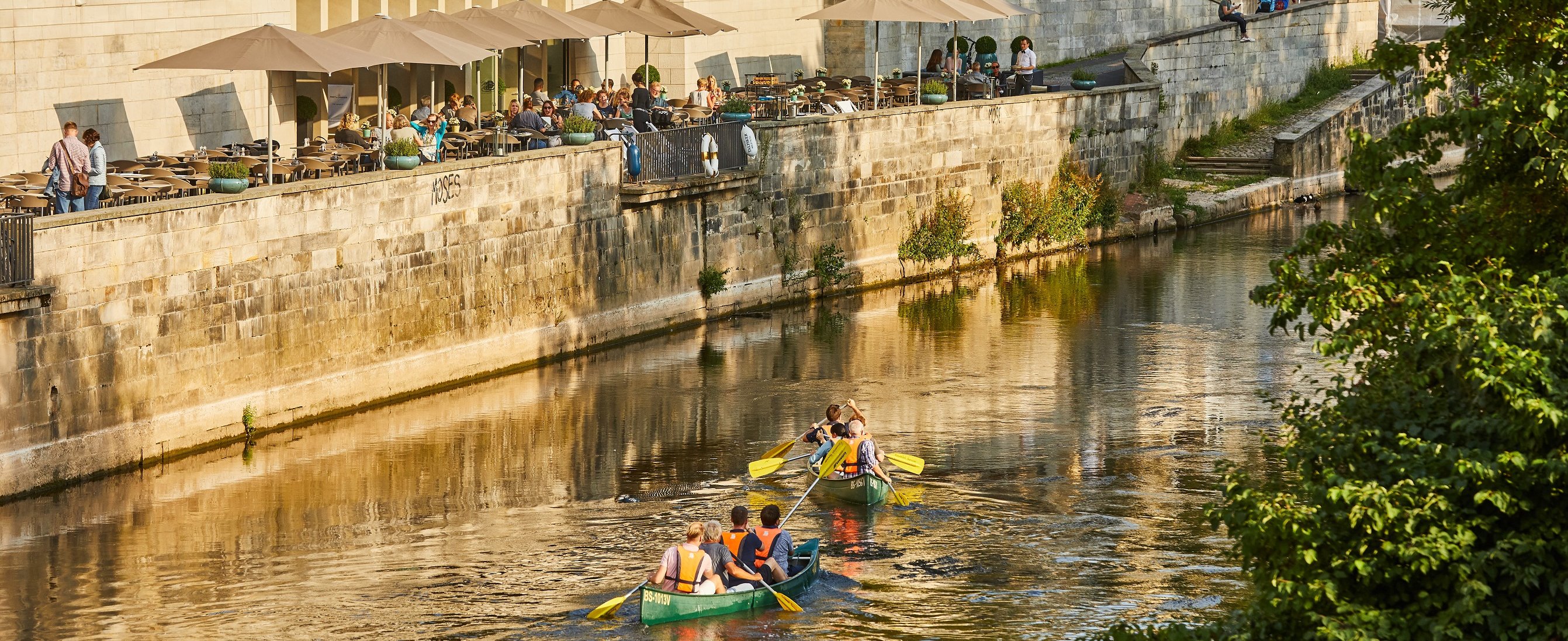 Two canoes with several people are floating on a river that runs through the old town of Hanover.