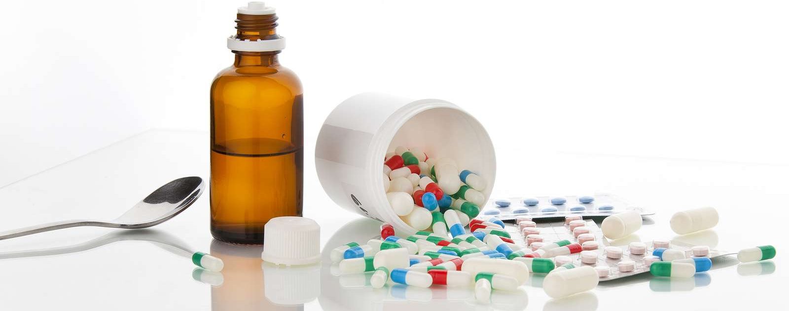 Symbolbild mit Löffel, einer Medikamentenflasche und vielen bunten Tabletten