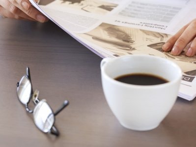 Zeitung, Kaffeetasse und Brille auf einem Tisch liegend