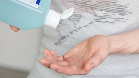 In eine offene Hand wird Flüssigkeit aus einer Plastikflasche geschüttet.