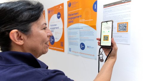 Dr. Maria Ines Cartes steht vor einem Poster mit einem QR-Code. Diesen scannt sie mit ihrem Smartphone.