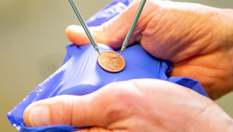 Tiny instruments of a microsurgical surgical robot surround a 5 cent coin. 