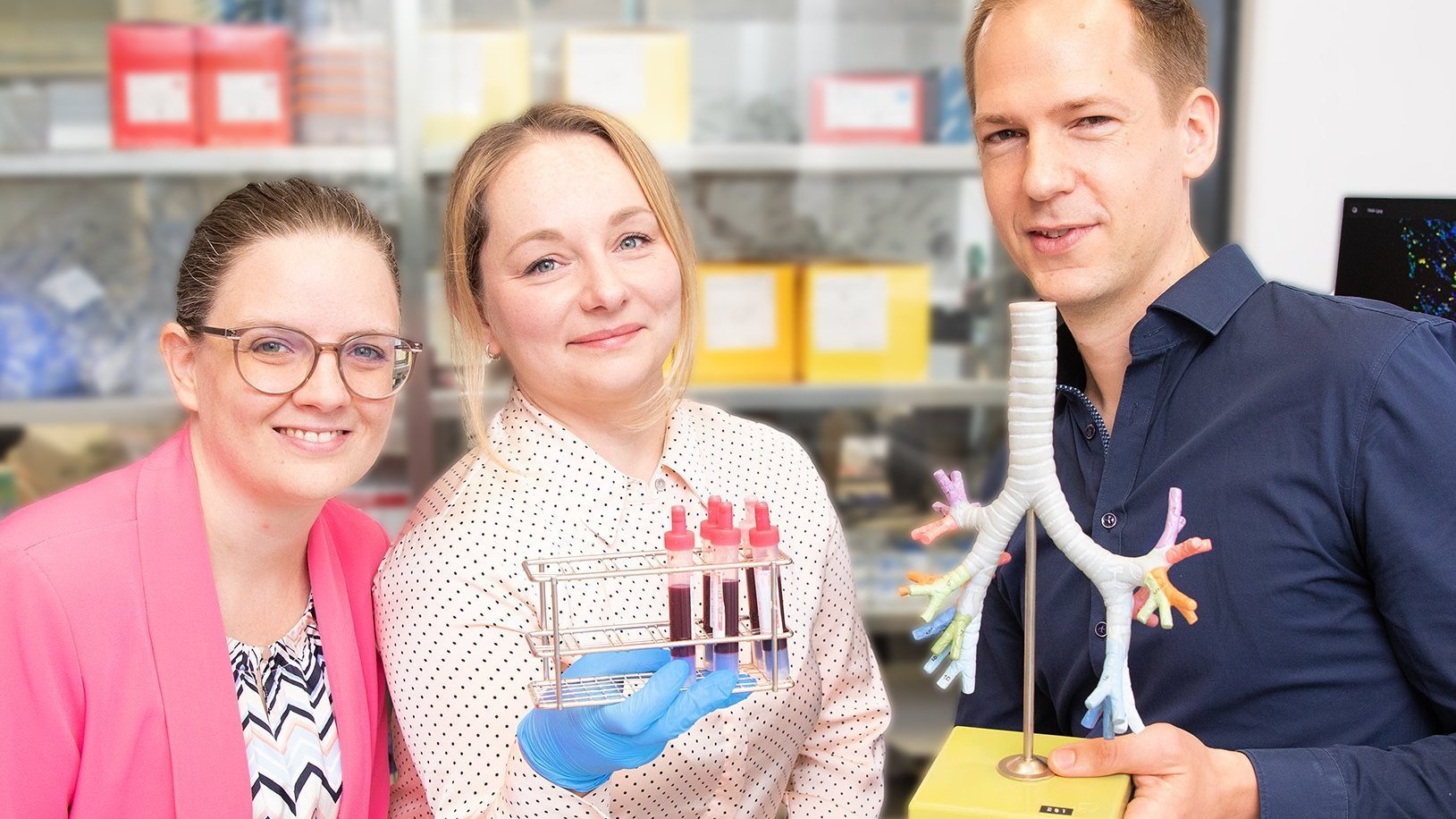 PD Dr. Lavinia Neubert, PhD student Edith Katharina Schwarz, and PD Dr. Jan-Christopher Kamp are standing in a laboratory and holding a lung model and blood samples in their hands.