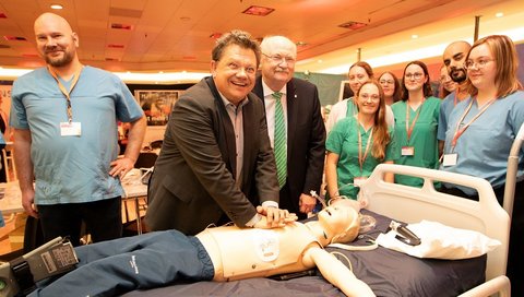 Gesundheitsminister Philippi und Prof. Manns stehen beim MHH-Event im aufhof an einem Patientenbett und reanimieren eine Puppe. 