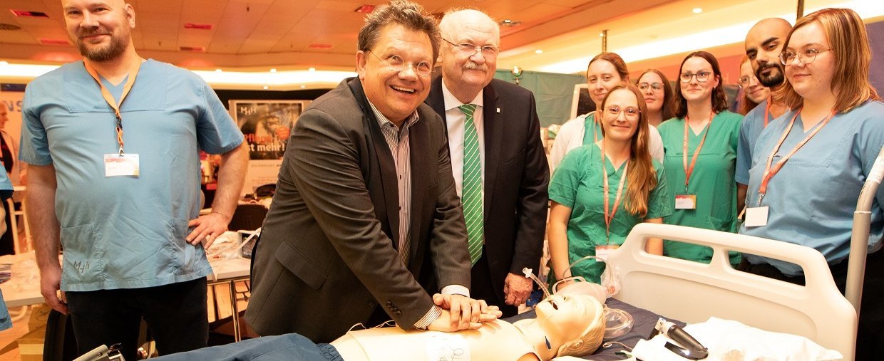 Gesundheitsminister Philippi und Prof. Manns stehen beim MHH-Event im aufhof an einem Patientenbett und reanimieren eine Puppe. 