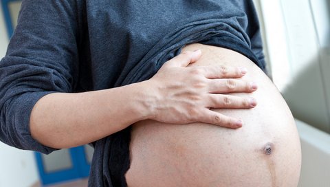 Eine schwangere Frau berührt ihren Bauch.