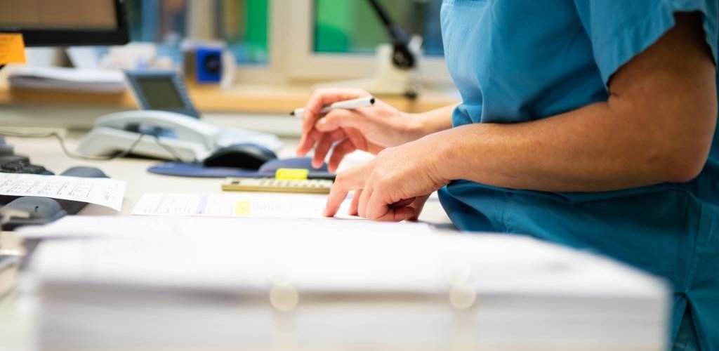 Eine Studynurse die sich im Studienbüro Notizen macht. Neben ihr liegt ein Ordner mit Dokumenten.