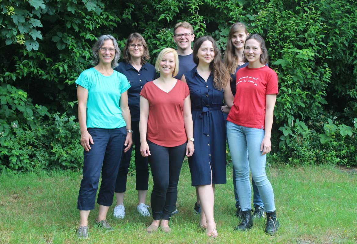 Gruppenfoto, 7 Personen auf einer Wiese vor Bäumen