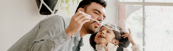 A man and a girl in a wheelchair are blowing bubbles together.