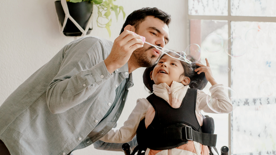 A man and a girl in a wheelchair are blowing bubbles together.