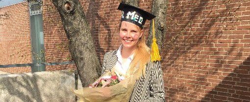 Einzelfoto von Carolin Sophie Berndt mit Doktorhut und Blumen in der Hand.