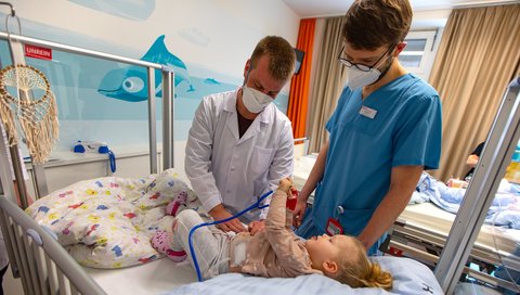 MHH-Student Niklas Oetzmann steht am Bett einer Patientin in der Kinderklinik und untersucht die Bauchdecke ihre Bauchdecke.