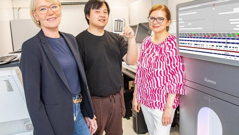 Drei Personen stehen neben einem modernen Laborgerät, auf dessen Bildschirm Analyseergebnisse angezeigt werden.