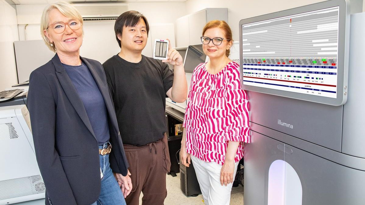 Three people are standing next to a piece of laboratory equipment, the screen of which displays analysis results. 