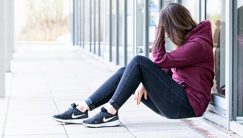 eine Frau mit dunklen Haaren sitzt auf dem Boden und stützt mit ihrer Hand ihren Kopf