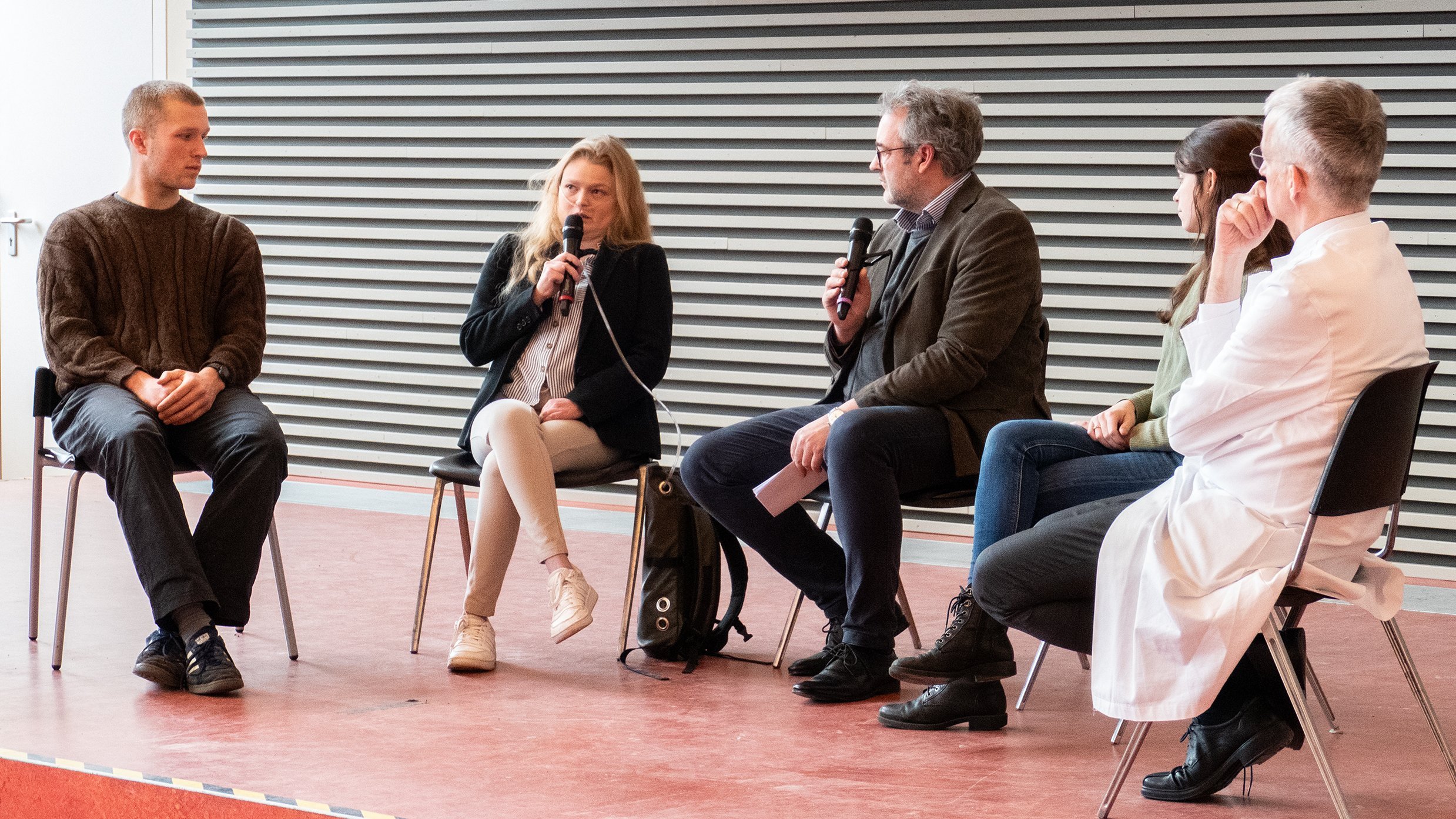 (v. l.) Malte Storsberg, India Heilmann, Prof. Dr. Christian Mühlfeld, Lina Rosenboom und Prof. Dr. Frank Lammert sitzen auf dem Podium eines Hörsaals. 