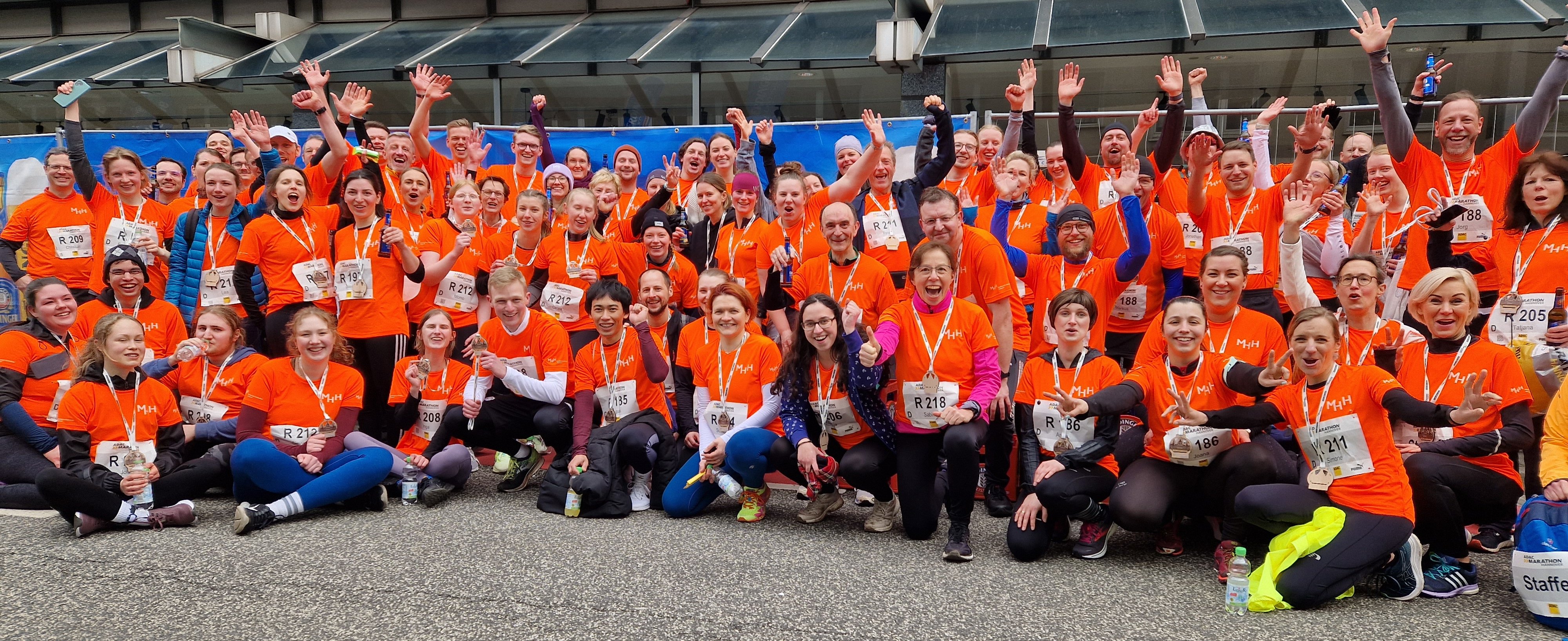 Mitarbeitende der MHH stehen für ein Gruppenfoto nach dem Hannover Marathon zusammen. Alle tragen orange farbene Trikots. 