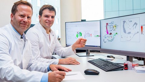 Clinic director Professor Schmidt-Ott (left) and his senior physician Dr Christian Hinze sit at a table with two PC monitors and a keyboard.