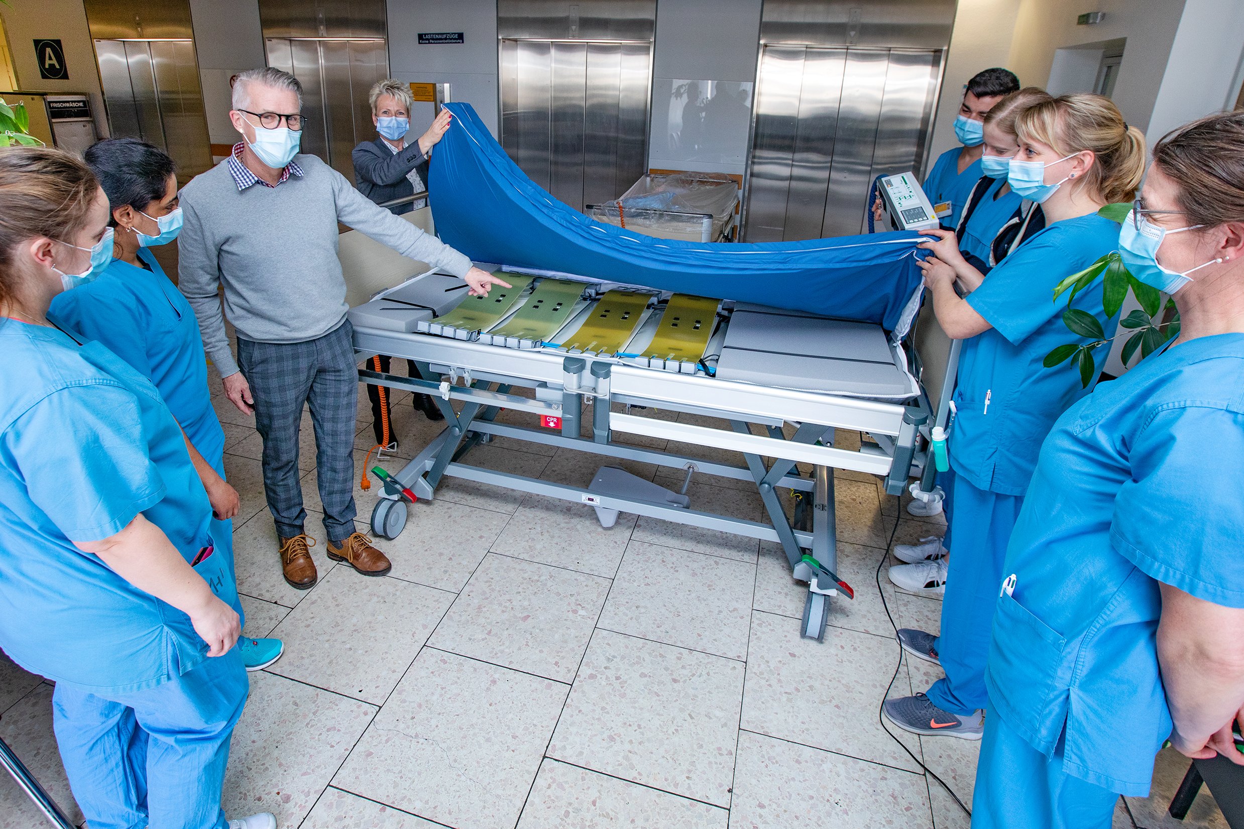© Karin Kaiser, MHH Mehrere Pflegekräfte heben die neu angeschaffte Matratze an. Der Mitarbeiter des Matratzenherstellers zeigt auf die komplexe Technik darunter, die die automatische Mobilisation ermöglicht.