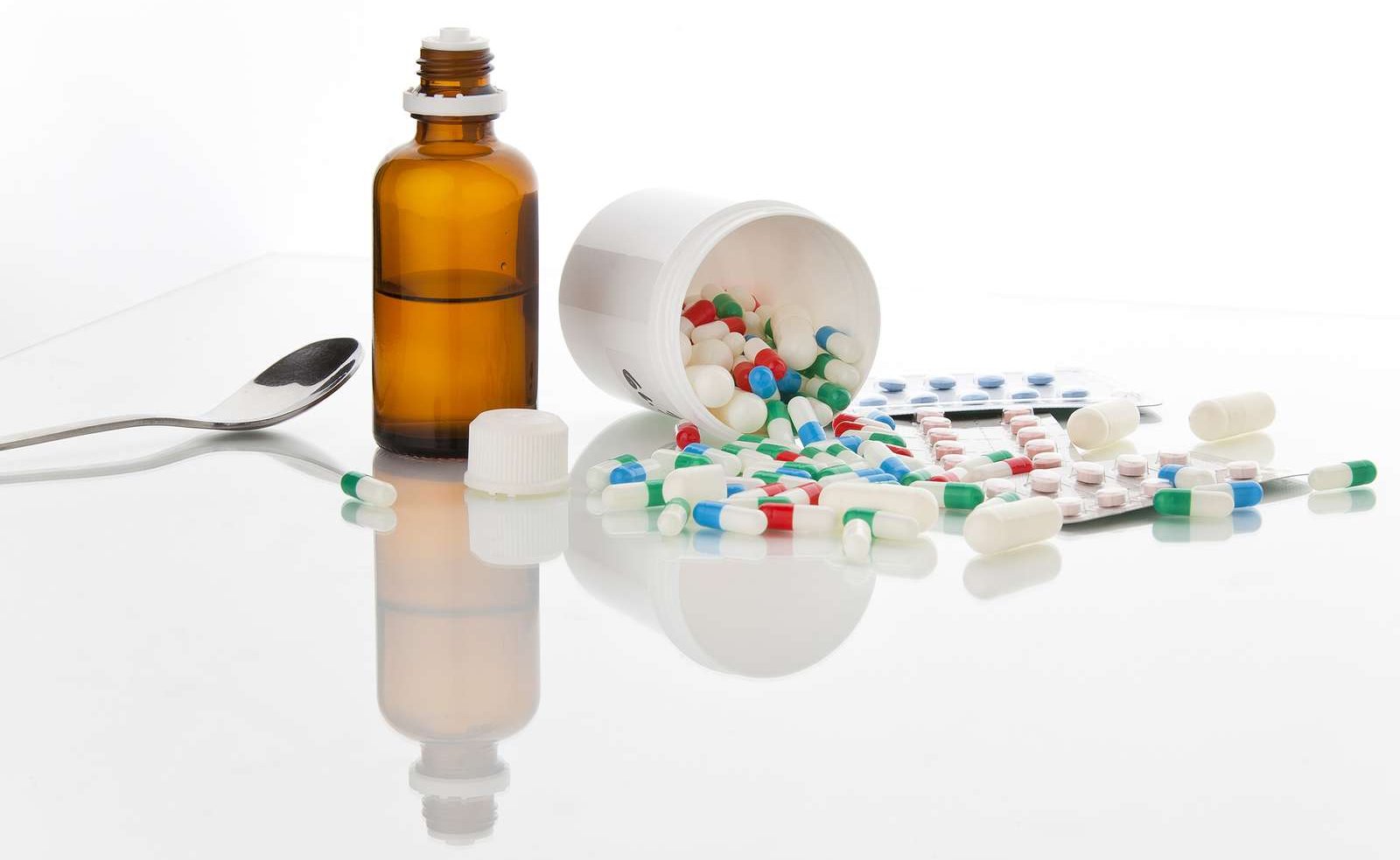 Ein Medikamentendöschen mit bunten Tabletten und ein Medizinfläschen, neben dem ein Löffel liegt.