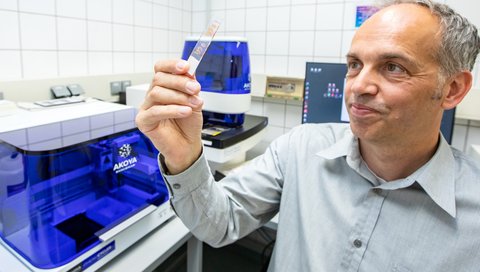 A man sits in a laboratory in front of a spectral microscope, holding slides in his hands.