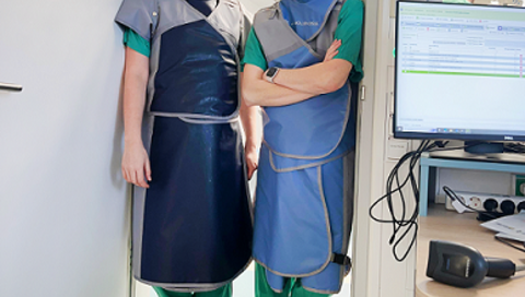  Dr. Henrike Hillmann (links) und Dr. Johanna Müller-Leisse tragen Schutzkleidung und stehen nebeneinander in einem Türrahmen. 