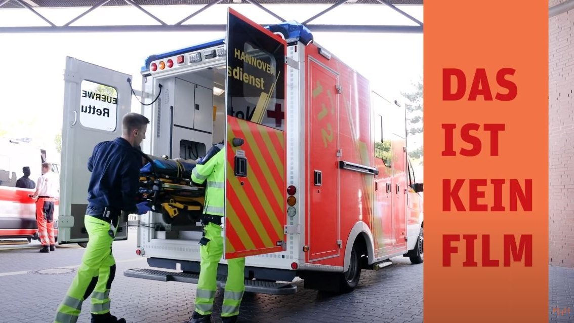 Aus einem Krankenwagen ziehen zwei Rettungskräfte eine Trage heraus. 
