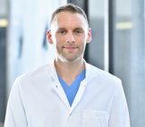 Porträtbild von Christoph Beier, der einen weißen Arztkittel trägt. 