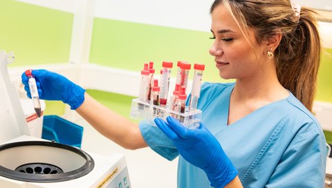 Eine junge Frau hält ein Röhrchen mit einer Blutprobe in der Hand. 