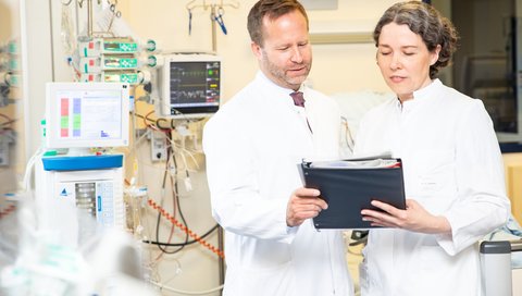 Professor Dr Kai Schmidt-Ott and Dr Vega Gödecke are standing in a room of the dialysis unit of the Clinic for Kidney and Hypertension Diseases and looking at a patient file.