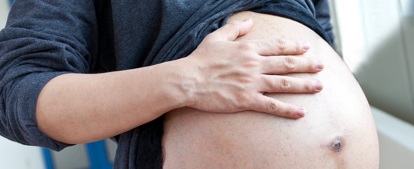 Der Bauch einer schwangeren Person, die eine Hand auf den Bauch liegen hat. 