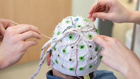 Two pairs of hands apply contact gel to the electrodes of an EEG cap.