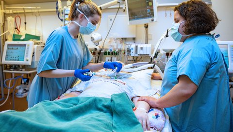 Two nurses in an intensive care unit at the bedside of a patient.